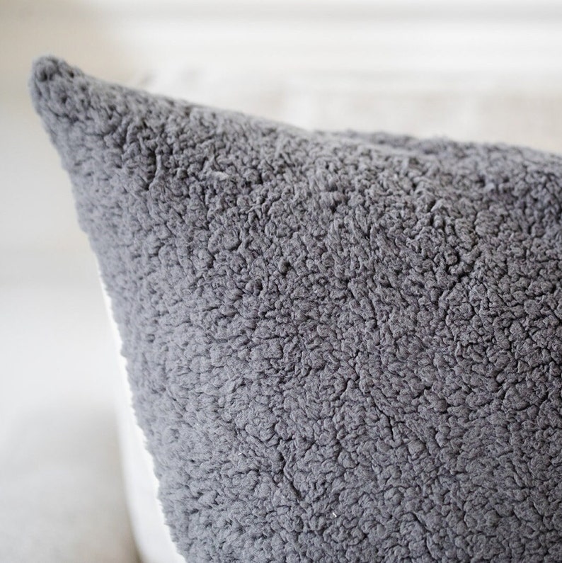 May include: Close-up of a gray, textured pillow. The pillow has a soft, plush appearance with a dense, fuzzy surface. The color is a muted gray, and the texture suggests a cozy, comfortable feel. The pillow's corner is visible.