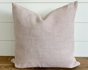 Puede incluir: Una almohada de tiro suave, de color marrón claro, con un tejido sutilmente texturizado. La almohada está hecha de una tela similar al lino y tiene un diseño simple y discreto.
