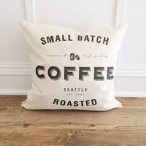 May include: A white pillow with black text that reads "SMALL BATCH", "mastery of high quality COFFEE", "SEATTLE EST. 1962", and "ROASTED".