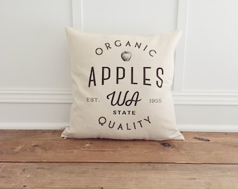 Puede incluir: Una almohada blanca con un diseño gráfico en blanco y negro que dice "Organic Apples WA State Quality" con una ilustración de manzana. El texto también incluye "Est. 1955".