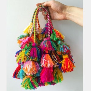 May include: A bunch of colourful yarn tassels with long strings. The tassels are made of different colours of yarn, including red, orange, yellow, green, blue, purple, and pink.