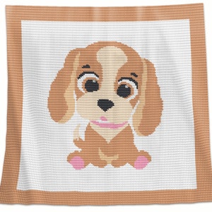 Può includere: Una coperta all'uncinetto con un cucciolo marrone e bianco con dettagli rosa. Il cucciolo è seduto con le zampe incrociate e ha un grande sorriso.