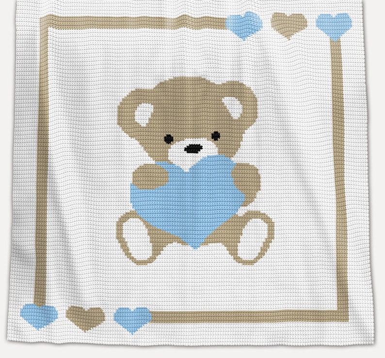 May include: A white crocheted baby blanket with a brown teddy bear holding a blue heart. The blanket has a brown border with blue and brown hearts.