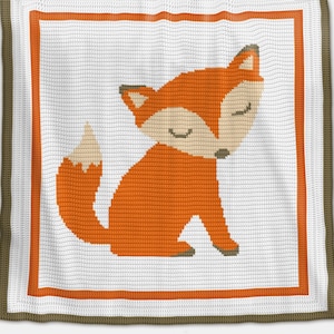 Puede incluir: Una manta de bebé de crochet con un diseño de zorro. El zorro es naranja con la cara blanca y la barriga blanca. La manta es blanca con un borde marrón y un borde interior naranja.