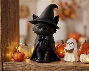 Peut inclure: Une figurine de chat noir portant un chapeau de sorcière pointu et une cape avec un nœud papillon, placée à côté d'une petite figurine de fantôme blanc tenant un livre ouvert, entourée de citrouilles orange et blanches et de guirlandes lumineuses.