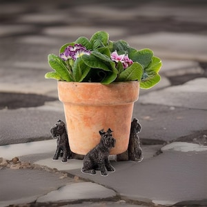 以下が含まれることがあります： 3体のダークグレーの質感のある犬のフィギュアに支えられたテラコッタ製の植木鉢。鉢には緑の葉の植物と小さな紫とピンクの花が入っています。犬のフィギュアは座った姿勢で彫刻されており、鉢の脚として機能しています。