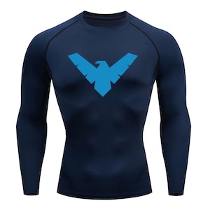 Op de afbeelding: Een donker marineblauw compressieshirt met lange mouwen en een felblauw gestileerd vogel-embleem in het midden op de borst. Het kledingstuk heeft een ronde hals en raglanmouwen met zichtbare zwarte stiksels langs de schoudernaden.
