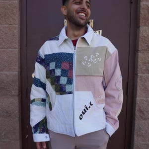 May include: A patchwork zip-up jacket featuring a mix of white, pink, and floral patterned fabric panels. The front includes a white collar, a small white heart graphic, and the text "oui.c" printed in black on the lower left side panel.