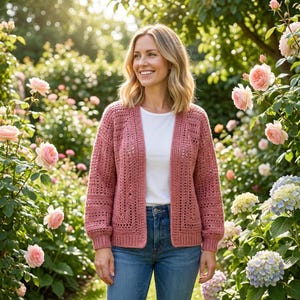 May include: A dusty rose open-front crochet cardigan featuring a textured geometric stitch pattern, long sleeves with ribbed cuffs, and a straight hemline, worn over a plain white t-shirt and blue denim jeans.