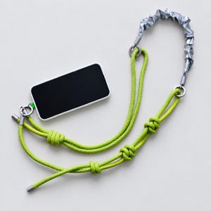 May include: A smartphone attached to a lime green rope lanyard featuring a silver metallic scrunchie-style section. The rope is secured with silver-toned metal end caps and circular rings, and includes three decorative knots along its length.
