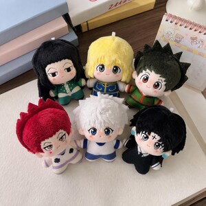 Pu&ograve; includere: Una collezione di sei bambole di peluche che raffigurano personaggi anime stilizzati con diversi colori di capelli, tra cui nero, giallo, verde scuro, rosso, bianco e nero. Ogni bambola ha grandi occhi ricamati, una piccola bocca e abiti unici.
