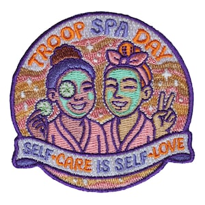 May include: A circular embroidered patch featuring two figures in pink robes with green facial masks. The text TROOP SPA DAY is arched at the top, and a banner at the bottom reads SELF-CARE IS SELF-LOVE. The background is a wavy peach and gold pattern.