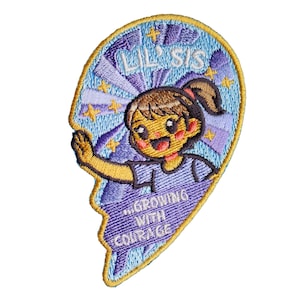 May include: A heart-shaped embroidered patch with a gold border featuring a cartoon character with brown hair in a ponytail. The design includes light blue and purple rays, yellow stars, and the text LIL' SIS and ...GROWING WITH COURAGE.
