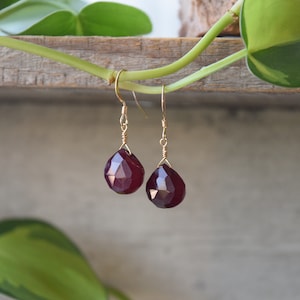 May include: A pair of dangle earrings with a deep burgundy gemstone drop on each earring. The earrings are made with gold wire.