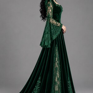May include: A floor-length dark green velvet gown featuring long flared lace sleeves, a square neckline, and a high side slit that reveals a beige lace panel. The dress is adorned with intricate green lace trim along the sleeves and skirt hem.