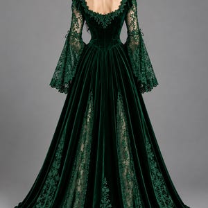 May include: A floor-length dark green velvet gown featuring long bell sleeves with intricate lace detailing, a square neckline, and a full skirt with lace-trimmed panels. The back of the dress displays a fitted bodice and a sweeping hemline.