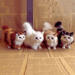 May include: Four small, fluffy plush cat figurines standing in a row. From left to right, the cats are orange and white, solid white, light brown and white, and dark brown and white. A vertical ruler shows a height of approximately 23 cm.