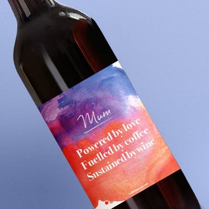May include: A wine bottle with a colorful label that reads "Mum Powered by love Fuelled by coffee Sustained by wine".