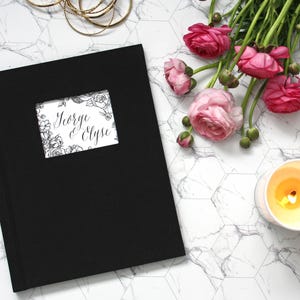 May include: Black fabric-covered album with a white window showing a floral design and the text "George & Elyse".