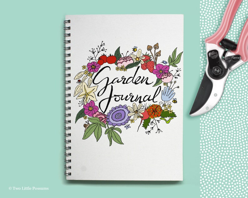 May include: A white spiral bound journal with a floral design and the text "Garden Journal" in black cursive lettering.
