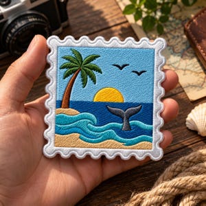May include: A square embroidered patch shaped like a postage stamp featuring a tropical beach scene. The design includes a palm tree on a sandy shore, a yellow sun, blue ocean waves, and a grey whale tail emerging from the water under two black birds.