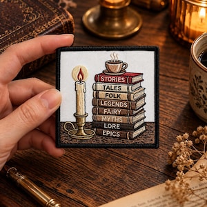 Può includere: Una toppa quadrata ricamata raffigurante una candela accesa in un supporto dorato accanto a una pila di otto libri sormontata da una tazza di caffè fumante. I dorsi dei libri riportano le parole STORIES, TALES, FOLK, LEGENDS, FAIRY, MYTHS, LORE ed EPICS.