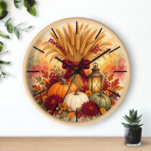 May include: A round wall clock with a light wood frame featuring an autumn-themed illustration of wheat stalks, a dark red bow, a lit lantern, pumpkins in orange, white, and green, and deep red flowers with black clock hands.