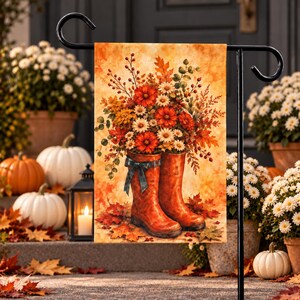 Peut inclure: Un drapeau de jardin rectangulaire présentant une illustration automnale vibrante de deux bottes en caoutchouc orange remplies d'un bouquet de fleurs orange et blanches, de baies et de feuilles d'automne, avec un ruban bleu sarcelle.