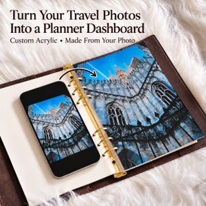 May include: A custom acrylic planner dashboard featuring a travel photo of a cathedral, displayed inside a brown leather binder with gold rings. The text reads: Turn Your Travel Photos Into a Planner Dashboard. Custom Acrylic • Made From Your Photo.