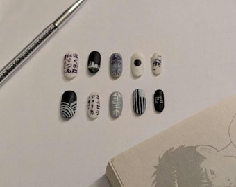 May include: Ten oval-shaped press-on nails featuring black, white, and gray hand-painted designs including Japanese characters, fish skeletons, stripes, and a solid circle, accompanied by a thin metal nail art brush and a sketchbook with a portrait.