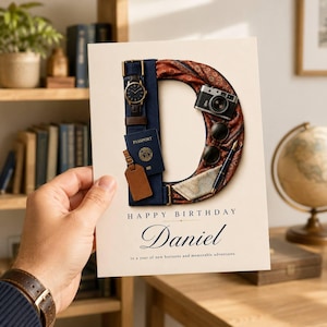 May include: A birthday card featuring the letter D formed by travel items including a wristwatch, passport, luggage tag, camera, sunglasses, pen, and map. The card displays the text Happy Birthday, the name Daniel, and a travel-themed message.
