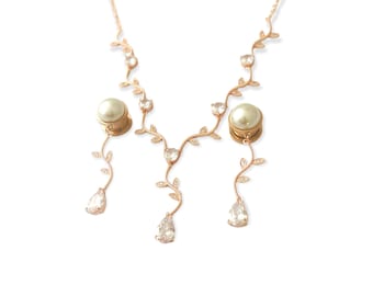 May include: A rose gold necklace and earrings set with a delicate vine design and pearl accents. The necklace features a chain with small leaves and clear crystals, while the earrings have a dangling pearl and crystal drop.