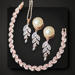 May include: A rose gold jewelry set with a delicate leaf design. The set includes a necklace, bracelet, and a pair of earrings with pearl accents.