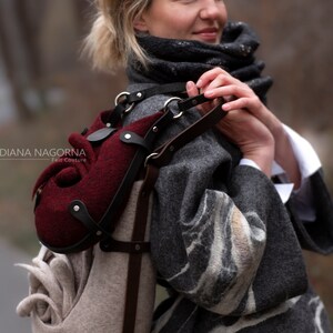 Puede incluir: Una mujer lleva un abrigo gris y blanco con estampado y lleva un bolso de fieltro &uacute;nico con una bolsa de fieltro burdeos adjunta. El bolso tiene una correa de cuero marr&oacute;n y herrajes plateados. El bolso est&aacute; dise&ntilde;ado con una forma org&aacute;nica &uacute;nica.