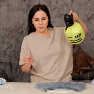 Puede incluir: Una persona sostiene un pulverizador de pl&aacute;stico amarillo con la etiqueta "3.0 Л" y "Дезинфицирующее средство". La persona est&aacute; de pie frente a una mesa con un trozo de tela azul sobre ella.