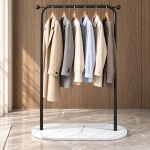 Puede incluir: Un perchero de metal negro con una base ovalada de patrón de mármol blanco. El perchero sostiene seis perchas de madera con varias prendas, incluyendo un abrigo beige, un blazer gris, un suéter crema, una camisa de rayas azules y un suéter marrón.