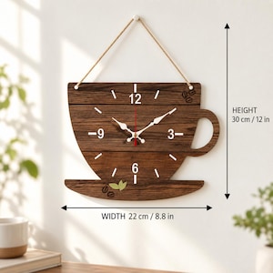 Puede incluir: Un reloj de pared de madera marrón oscuro con forma de taza de café con asa y platillo. La esfera muestra los números blancos 3, 6, 9 y 12, manecillas blancas y detalles de granos de café. Mide 30 cm de alto y 22 cm de ancho.