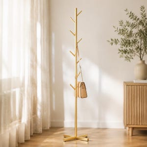 Puede incluir: Un perchero de metal dorado, alto y esbelto, con un poste central vertical y varias ramas en ángulo para colgar objetos. Un bolso de mano de color beige claro con una fina correa de cadena dorada cuelga de una de las ramas centrales.