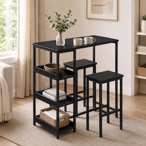 May include: A black rectangular bar table with two matching stools and three integrated side shelves. The table surface holds a clear glass vase with green eucalyptus stems and two white ceramic mugs. Two woven baskets and books sit on the shelves.
