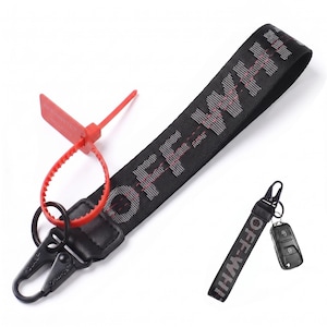May include: A black fabric keychain strap featuring the white text OFF-WHITE with red stitching details. It includes a black metal lobster clasp, a red plastic zip tie security tag, and a smaller matching keychain attached to a black car key fob.