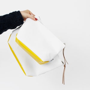 Pu&ograve; includere: Due pochette con cerniera bianche con bordino giallo. La pochette pi&ugrave; grande ha la scritta "REFILL" stampata sul fondo. Le pochette sono tenute in una mano.