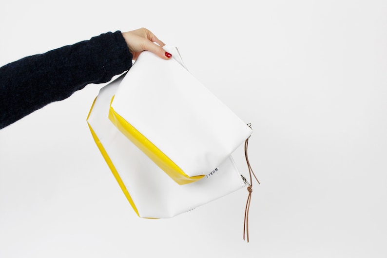 Pu&ograve; includere: Due pochette con cerniera bianche con bordino giallo. La pochette pi&ugrave; grande ha la scritta "REFILL" stampata sul fondo. Le pochette sono tenute in una mano.