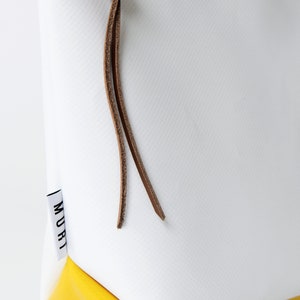 Pu&ograve; includere: Borsa bianca con cerniera, fondo giallo e cinturino in pelle marrone. La borsa ha la scritta "MURI" stampata sul lato.