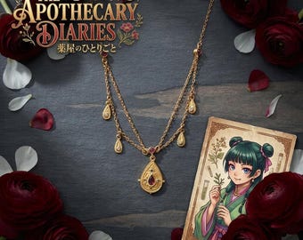 May include: A gold-toned double-chain necklace featuring a central teardrop pendant with a red stone and four smaller teardrop charms. The text The Apothecary Diaries is visible, alongside an illustration of a character holding a plant.