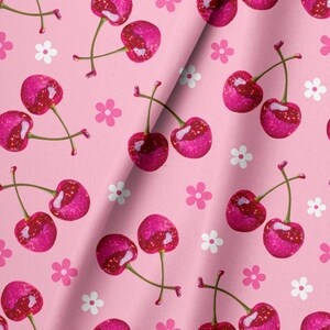 May include: A light pink fabric featuring a repeating pattern of vibrant magenta cherries with glittery textures and small white five-petaled flowers scattered throughout the design. The fabric has a soft fold running diagonally across the center.