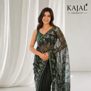 May include: A dark green saree featuring a sheer net fabric with intricate white and green floral embroidery along the scalloped borders and throughout the drape. The garment is paired with a sleeveless dark green blouse. Text reads KAJAL TRENDYFY.