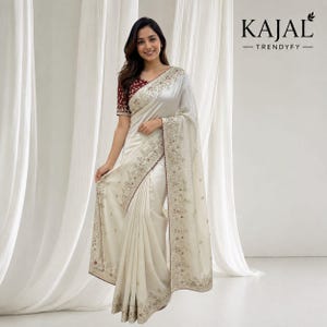 Könnte beinhalten: Ein cremeweißer Satin-Sari mit aufwendiger goldener und kastanienbrauner Blumenstickerei entlang der Ränder und einer passenden kastanienbraunen Bluse mit kurzen Ärmeln. Der Text KAJAL TRENDYFY ist oben rechts im Bild zu sehen.