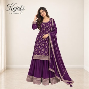 Könnte beinhalten: Ein tiefviolettes Sharara-Anzugset bestehend aus einer langärmeligen Tunika mit goldener Blumenstickerei, einem passenden ausgestellten Rock mit verziertem besticktem Saum und einem abgestimmten Dupatta mit Golddetails. Der Text Kajal TRENDYFY ist sichtbar.