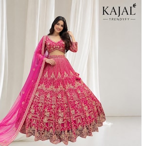 May include: A vibrant fuchsia lehenga choli set featuring intricate gold embroidery and sequin detailing throughout the skirt and blouse. The ensemble includes a matching sheer fuchsia dupatta with a gold border. Text KAJAL TRENDYFY is visible.