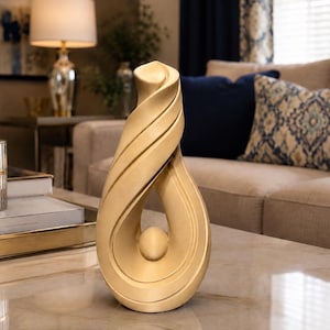 May include: A beige sculpture featuring a smooth, swirling, abstract form that curves upward to a point, with a small, spherical element suspended within the central open space of the structure, creating a continuous, fluid, and balanced design.